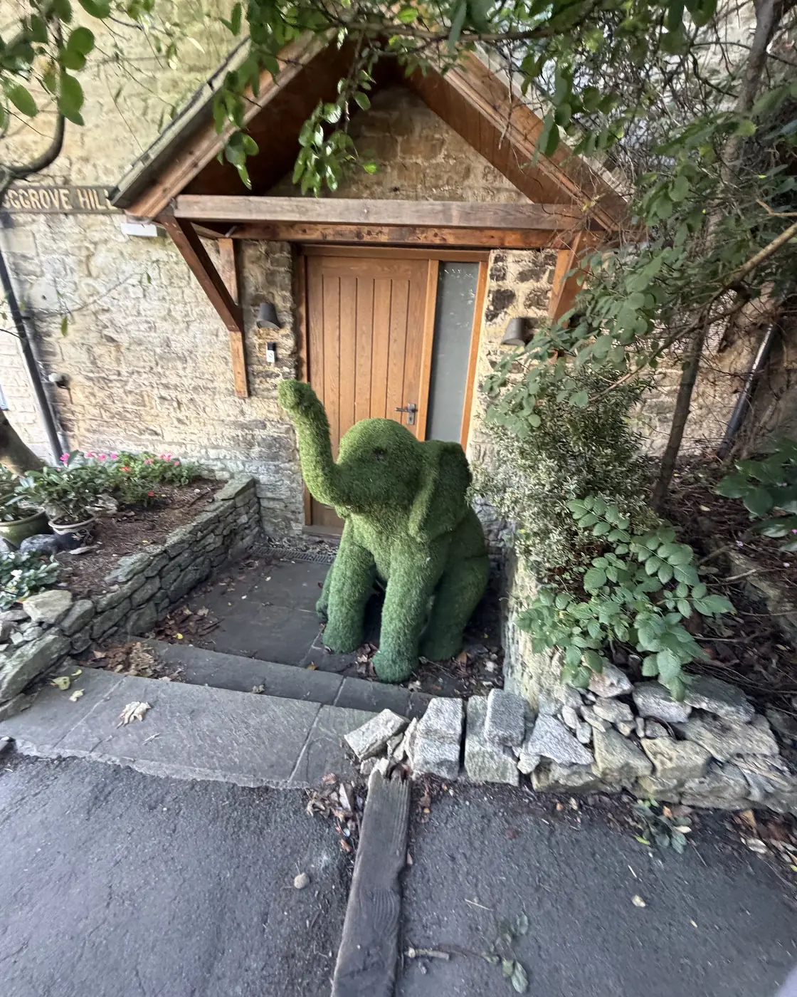 A green topiary elephant beside a wooden cottage door on Hoggrove Hill in Woodstock