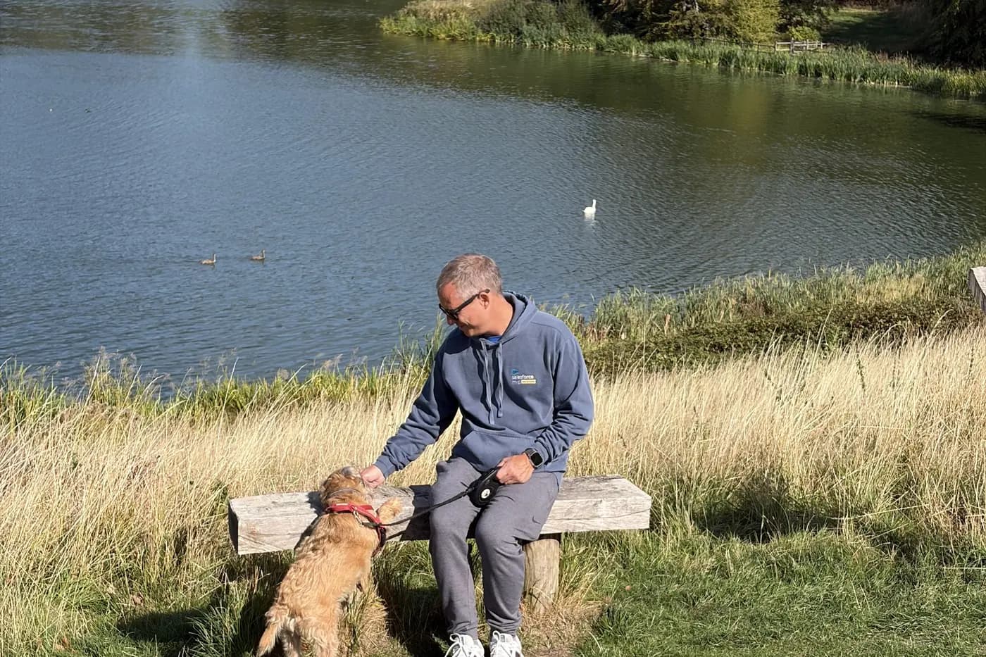 A man sitting on a bench by the lake at Blenheim, stroking Astro the border terrier